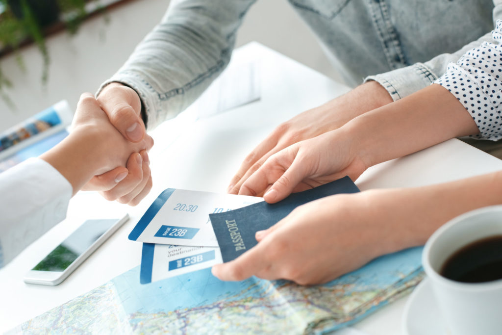 multiple hands of travel agents are holding passports and tickets that were booked for vacation with Jaya Travel.