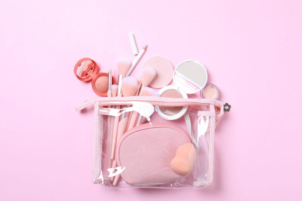 a bag full of makeup sitting on a pink background which displays the best products tips and hacks for traveling with makeup with Jaya Travel.