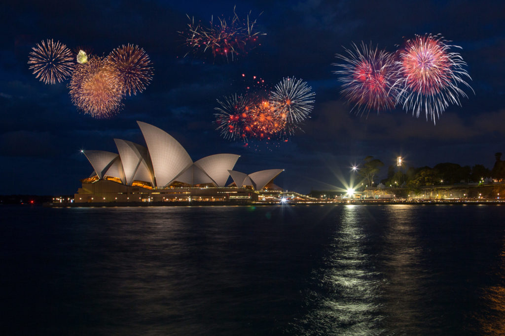 the sydney opera house in australia on New Year's Eve with bright fireworks exploding overhead which you can travel and tour with Jaya.
