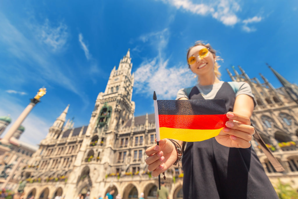 A female university student holds a German flag in front of the Munich city hall on a study abroad trip tour program.