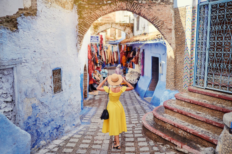 A young woman traveler in a yellow dress from Jaya Travel & Tours shopping the local stores in the medina of the blue city Chefchaouen in Morocco.