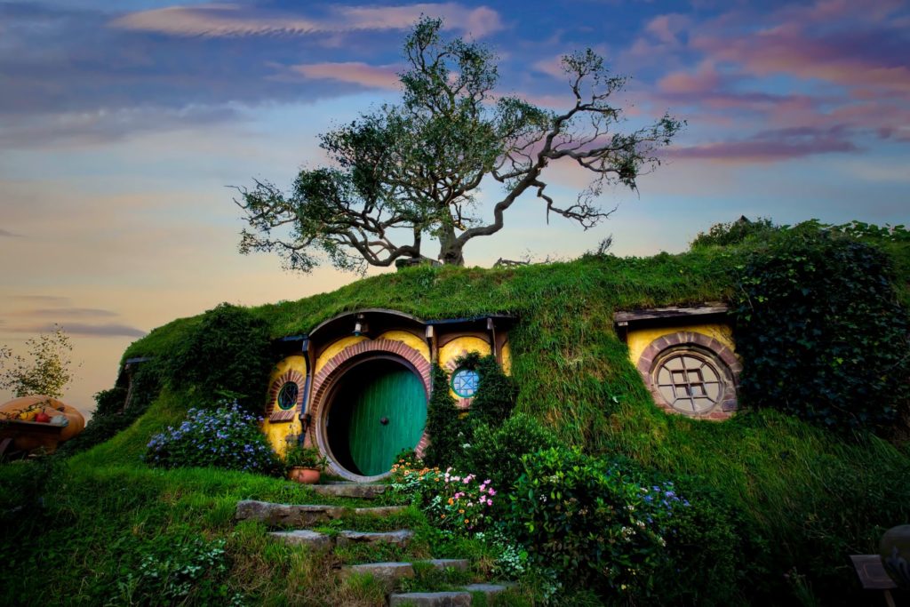 A tall, grassy hill is the walls of a Hobbit house in Hobbiton in New Zealand, Australia while the sky is darkened with a beautiful sunset. Jaya Travel & Tours travel blog post "On Location: The Lord of the Rings" lists the filming locations from Peter Jackson's popular movie and book trilogy.