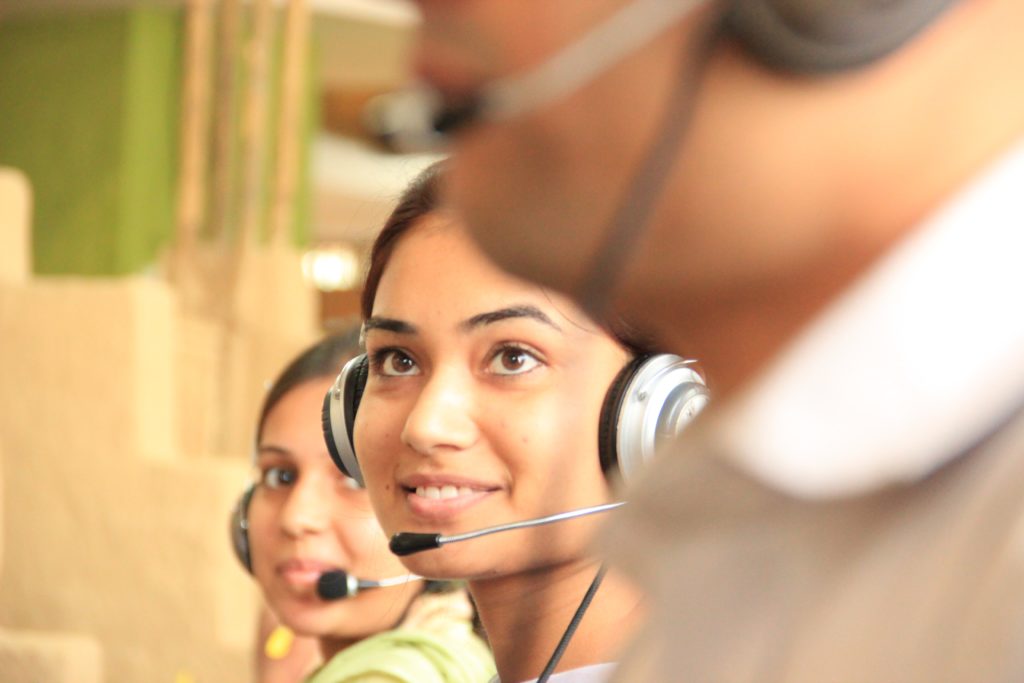 A portrait of a young woman wearing a headset and speaking on the phone at a Jaya Travel call center, where our customer service team works to help customers get travel help around the clock. This image is featured in the Jaya Travel & Tours blog, "Save more with Jaya travel agents"