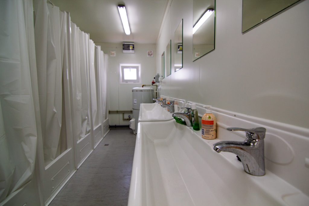 A very clean hostel bathroom with two large washing sinks and multiple small showers for guests to bathe on vacation for cheap. This image is featured in the Jaya Travel & Tours blog post, "Debunking 5 Myths About Hostels," which describes false lies about staying in a hostel on vacation and why they are incorrect.