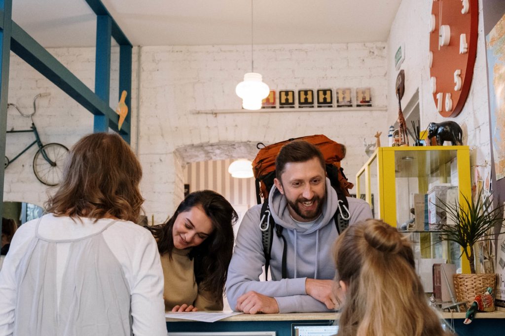 A middle-aged man and woman check into their hostel with front desk registration and look happy. This image is featured in the Jaya Travel & Tours blog post, "Debunking 5 Myths About Hostels," which describes false lies about staying in a hostel on vacation and why they are incorrect.