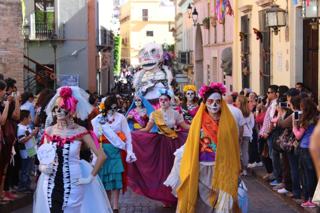 Featured in "Celebrate Halloween Around the World" Jaya Travel & Tours this image features a colorful Dia de los Muertos parade going through the streets of Mexico.