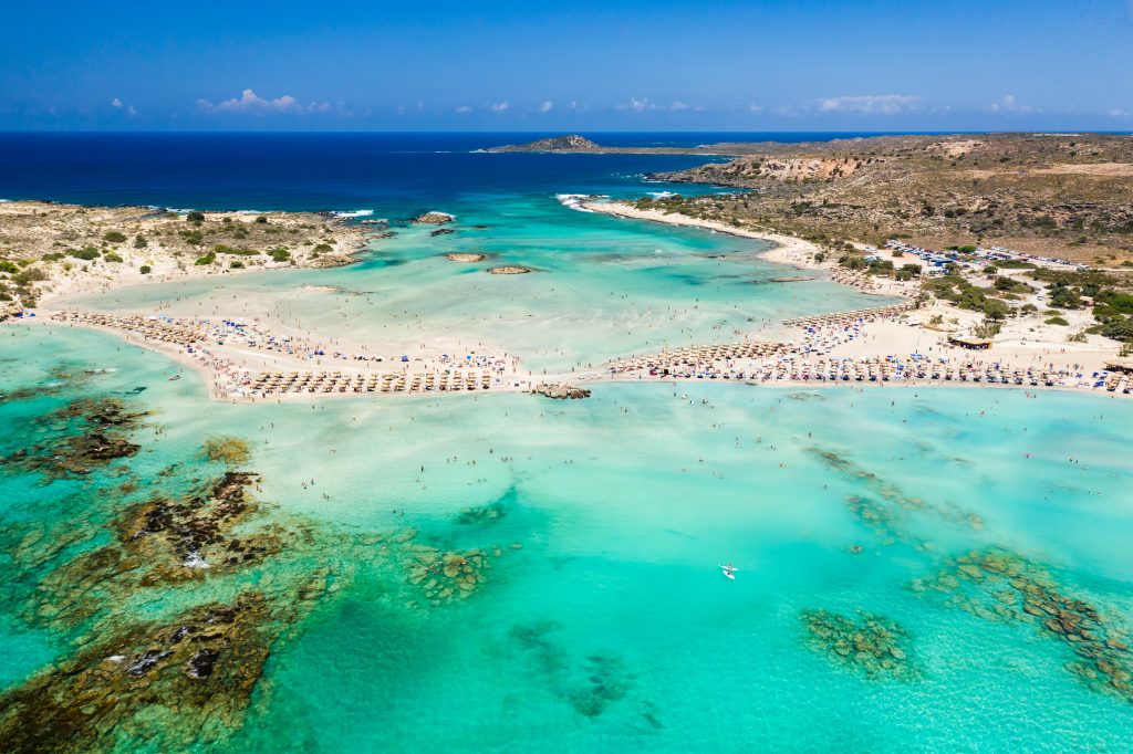 Jaya Travel & Tours blog Top 10 Destinations Aerial view of a beautiful but busy sandy beach and shallow lagoons surrounded by clear blue ocean Elafonissi Crete in the Peloponnese